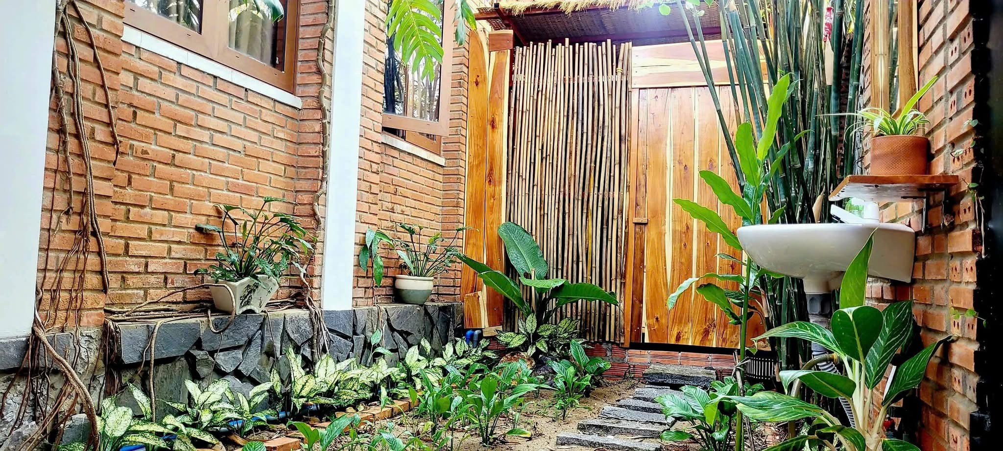 Góc vườn sau có bồn rửa gắn tường gạch, cổng tre và luống cây thấp